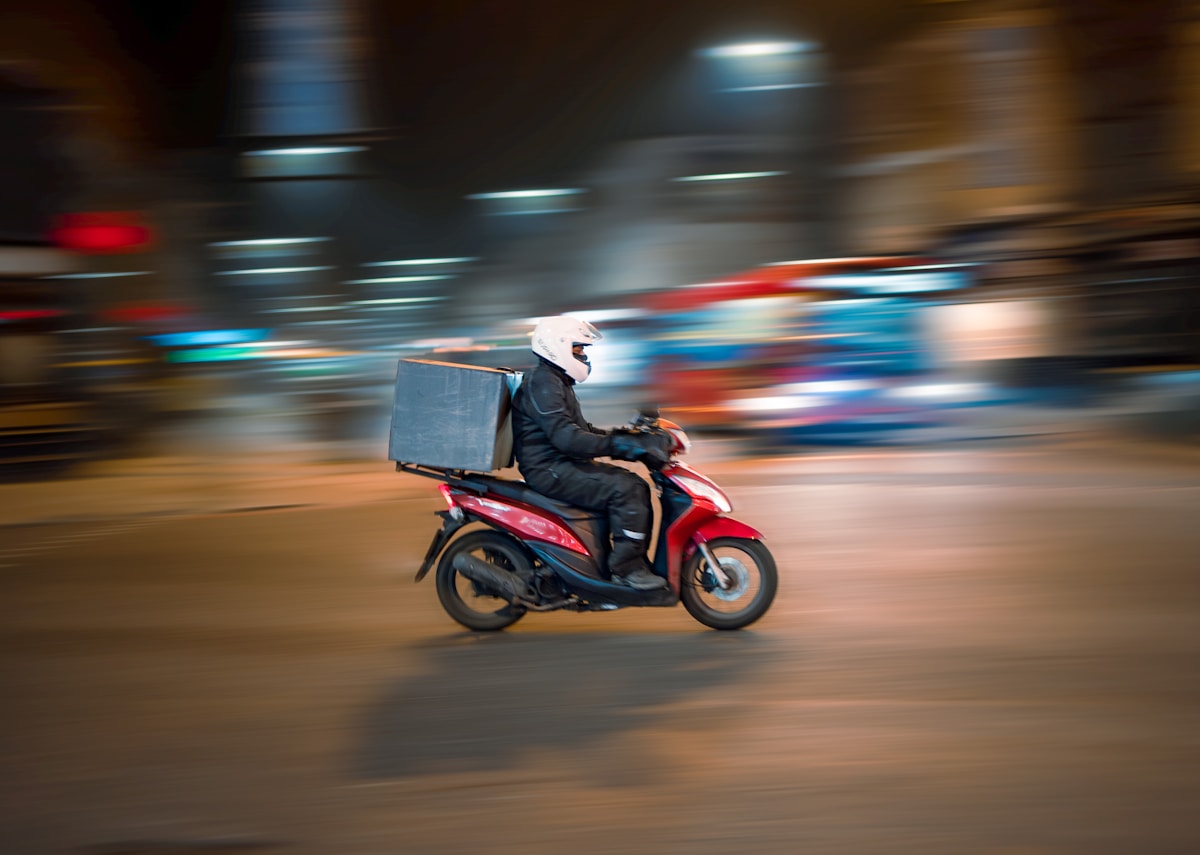 O que é delivery: entregador de moto com bag térmica levando pedido de restaurante à noite